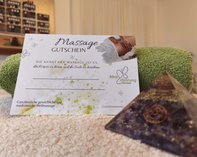 Massage-Gutschein von Körpererfahrung auf einer Massageliege, dahinter ein grünes Handtuch, vorne eine violette Kristallpyramide mit Kupferspirale